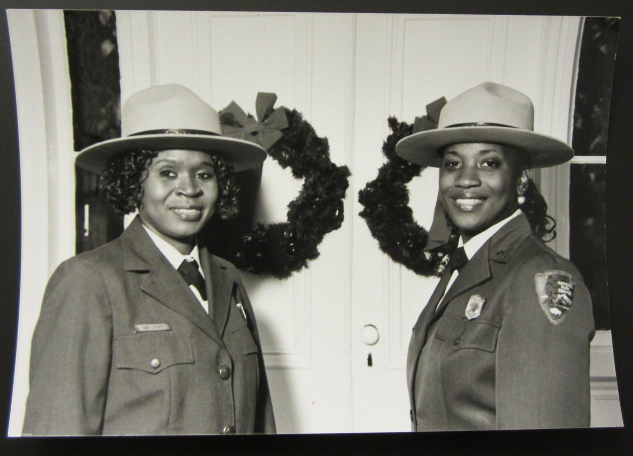Two African American women in NPS uniform stand in front of a double door with two wreaths