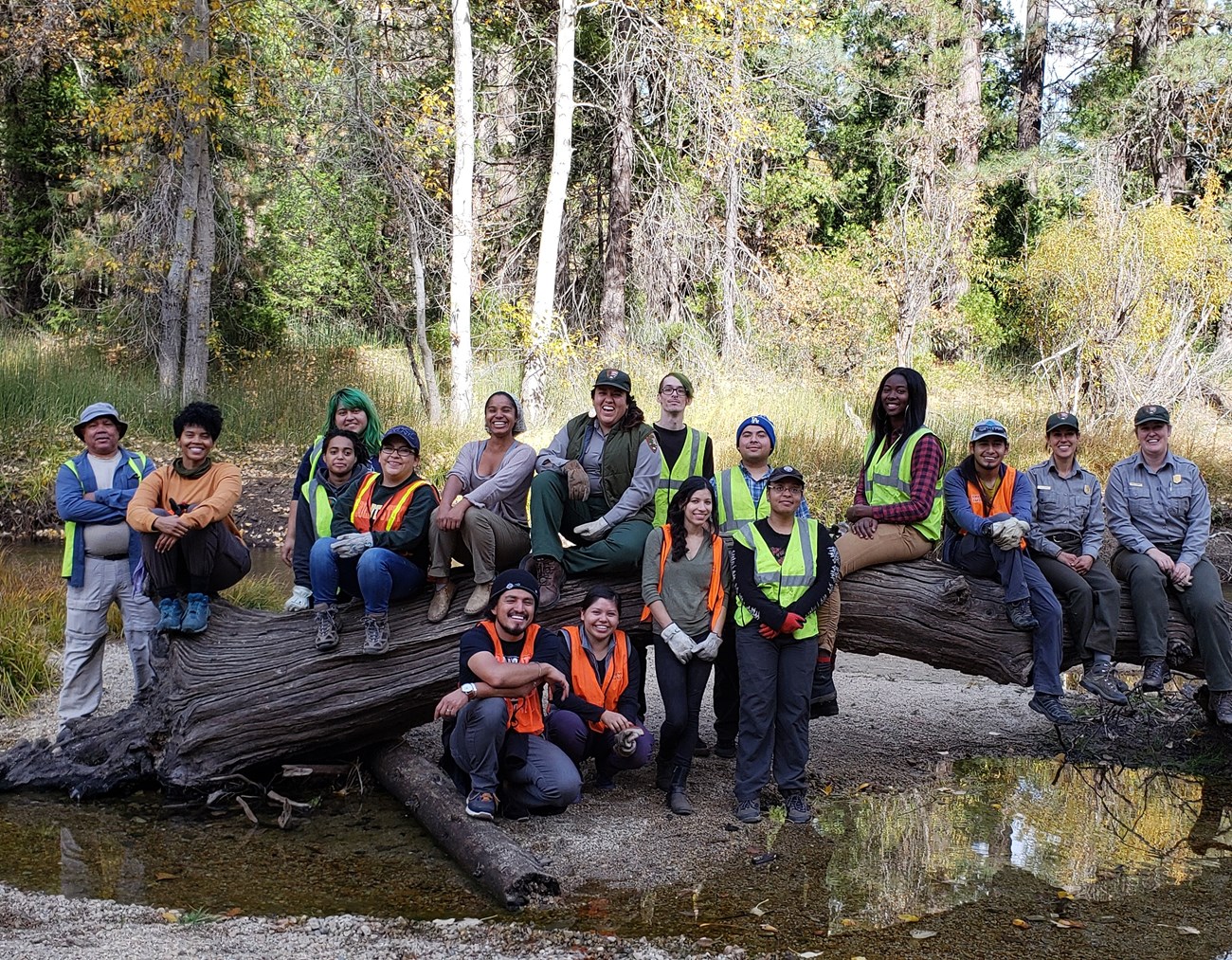 Participants in We.R.More, a workshop for ethnic and racial minorities in outdoor rec, pose on a large horizontal log in a shallow creek.