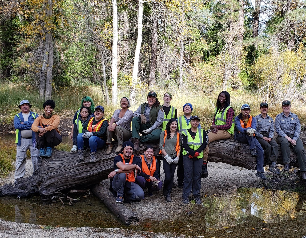 We.R.More and Building Bridges To The Outdoors Participants in We.R.More, a workshop for ethnic and racial minorities in outdoor rec, pose on a large horizontal log in a shallow creek.