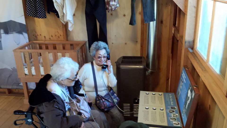 Maruki sisters listen to their oral history Two women hold phones to their ears in a museum exhibit inside a barracks