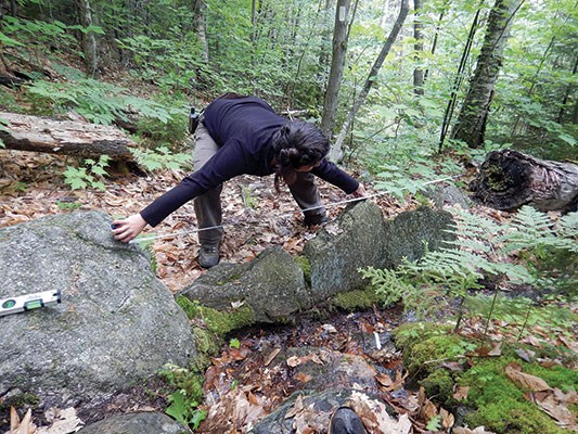 A woman measures the width of a trail drainage feature as part of the TDF assessment.