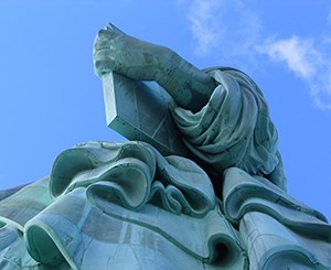 Lady Liberty's arm with tablet of law. Image credit: NPS Photo of a part of the Statue of Liberty with Lady Liberty's arm holding a tablet of law above her robe. A blue sky is above her.