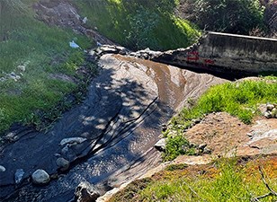 A dark, thick slurry of mud up against a dam with red markings indicating where intake and bypass pipes are buried.