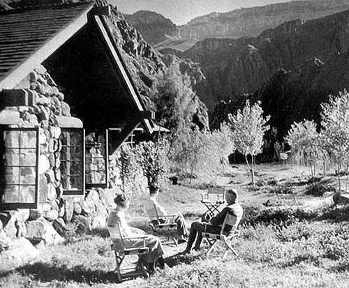 Three visitors sit outside the original lodge at Phantom Ranch around 1925. Shows view to the south with cottonwood trees.