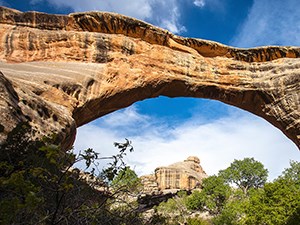 Photo of a colorful, natural stone bridge, framing a landscape with colorful rocks and trees.