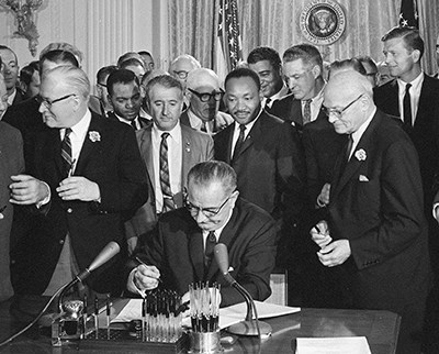 Signing of the Civil Rights Act of 1964 photo of Lyndon Johnson signing a document with Martin Luther King Jr and others standing behind him