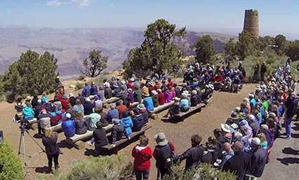 Approximately 100 participants attend the re-dedication ceremony of the Desert View Watchtower.   Participants are seated with a view of the Grand Canyon and the Desert View Watchtower.