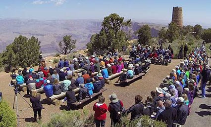 lt= Approximately 100 participants attend the re-dedication ceremony of the Desert View Watchtower. Participants are seated with a view of the Grand Canyon and the Desert View Watchtower.