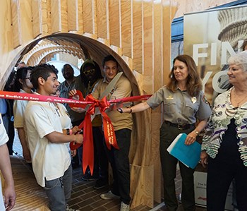 Anza Trail Parklet Ribbon-Cutting at Laney College Oakland, 2016 a student cuts a red ribbon assisted by a uniformed ranger