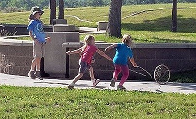 Three children play the hoop and stick game during Kids' Camp. Three children play the hoop and stick game during Kids' Camp.