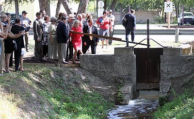 Members of the San Antonio Conservation Society, Senator Kay Bailey Hutchinson, and National Park Service employees lift the gate on the restored San Juan Acequia to allow water to flow.