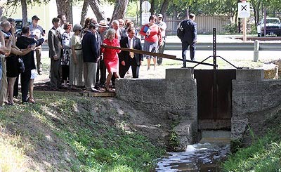 lt= Members of the San Antonio Conservation Society, Senator Kay Bailey Hutchinson, and National Park Service employees lift the gate on the restored San Juan Acequia to allow water to flow.