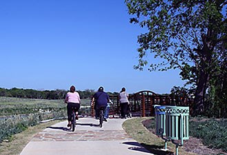 lt= Bikers biking along The Mission Riverwalk Hike and Bike Trail.