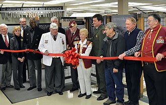 lt= Former Prisoners of War dedicate the traveling exhibit during a ribbon cutting event.