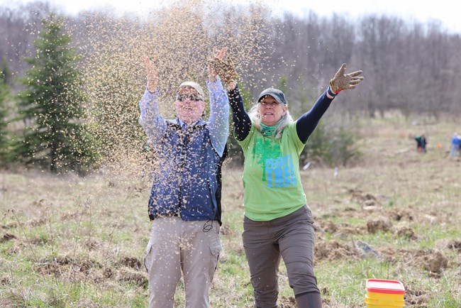 An older man and woman cast wildflower seeds in a field.