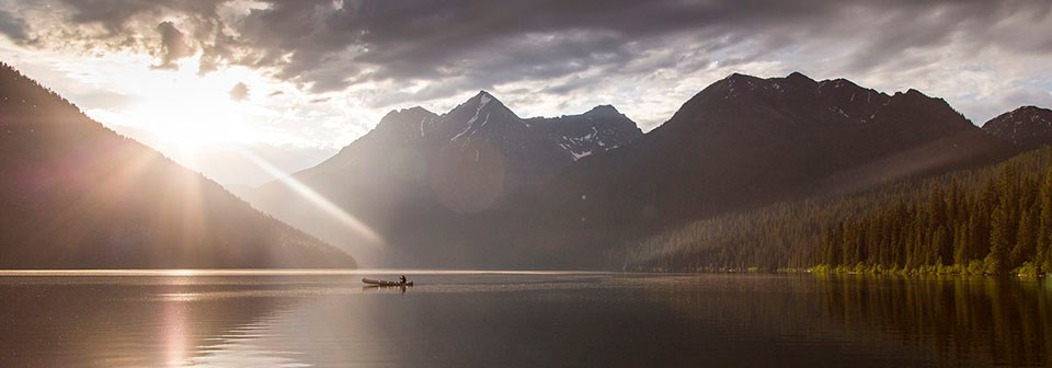 the sun begins to set as a canoe floats on a serene lake surrounded by mountains