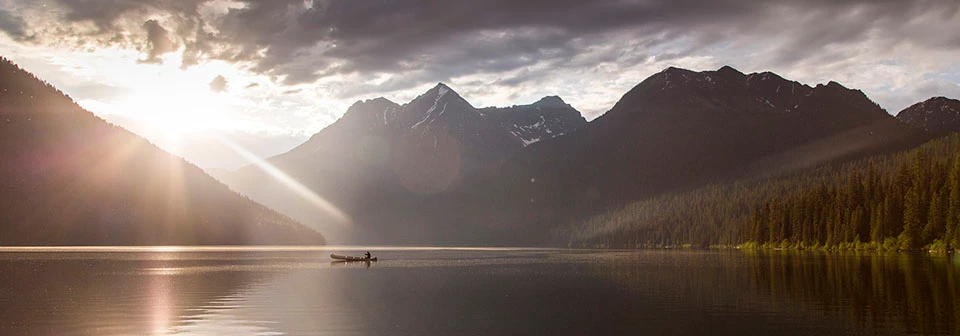 Fishing on Quartz Lake at Glacier National Park the sun begins to set as a canoe floats on a serene lake surrounded by mountains