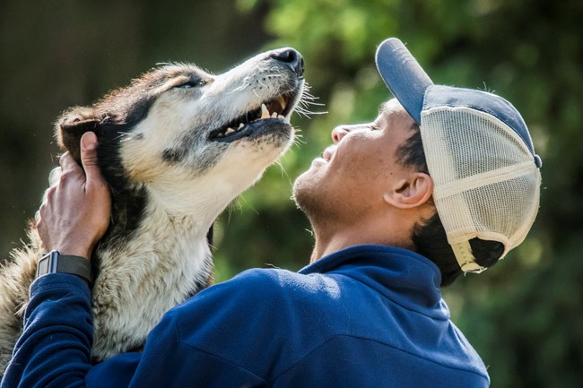 a smiling man in a hat pets a dog