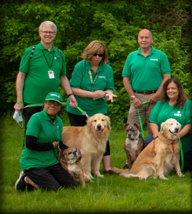 Five people in bright green shirts proudly stand by their pet ambassadors.