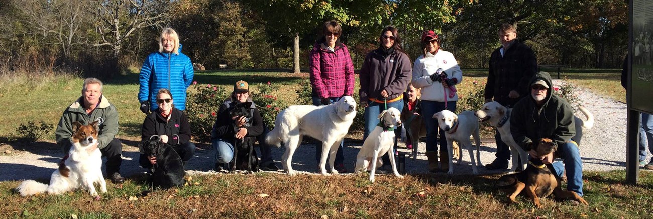 Nine people and their pets pose for a group photo on a fall day.