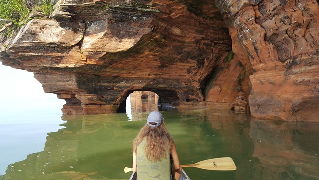 Canoe_HAB Gril canoes into a cave. Lake green with algae bloom.