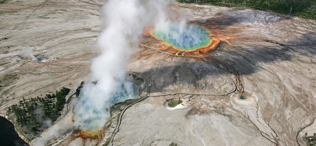 An aerial view of two rainbow colored hot springs giving off steam.