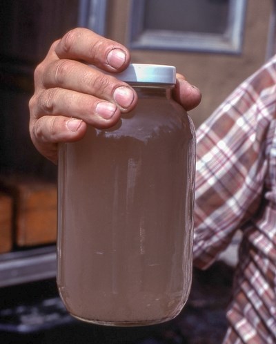 Sediment in Water Man holding jar filled with brown tinted water