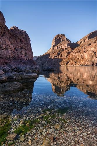 Different layers of sandstone in canyon walls reflected into water below.