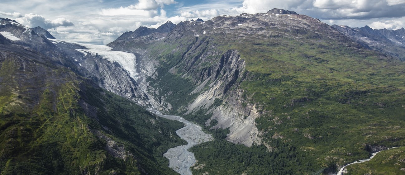 An aerial view of a stream emerging from a glacier high up in the mountains