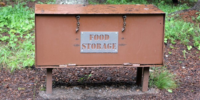 A brown metal bear-resistant food locker with sign that says "food storage."