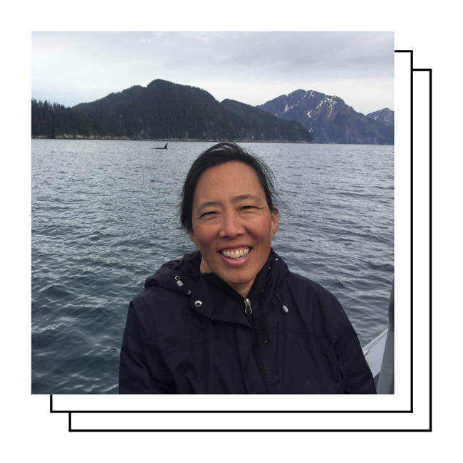 Sharon Kim WSR A smiling woman with dark hair and tan skin with the ocean, an orca fin, and mountains in the background