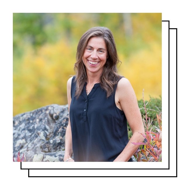 A smiling woman with medium length brown hair poses amid fall colors