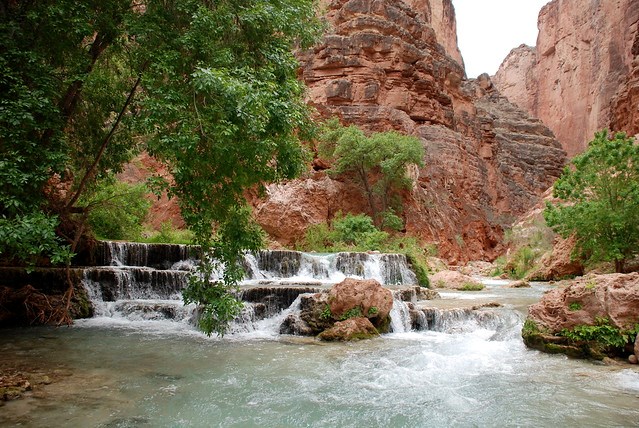 Havasu Creek River spilling over tiered rock formation below red rock canyon walls