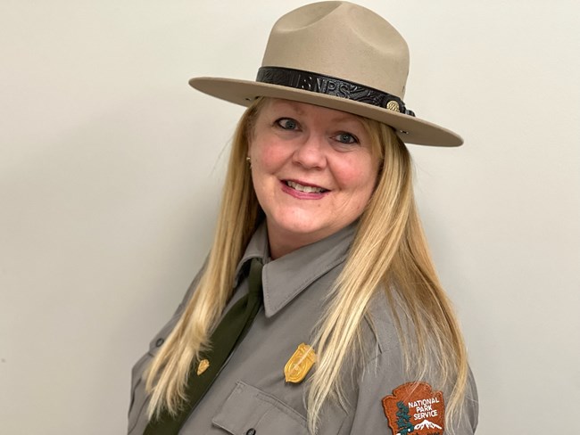 a smiling woman with long straight blonde hair wearing a national park service uniform and hat
