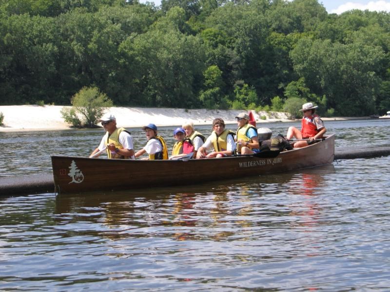 National Park Service Ranger and a group of children paddling in a large canoe.