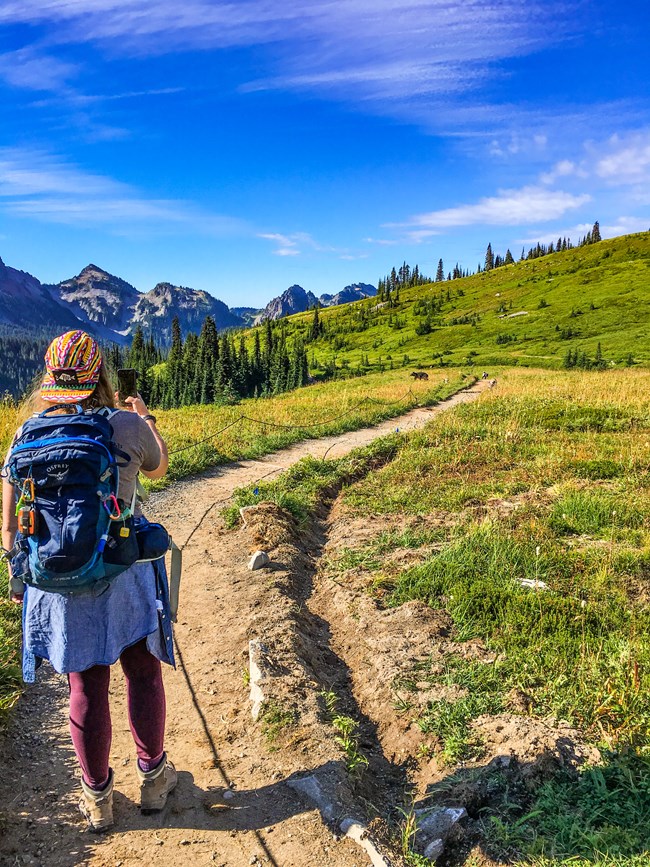 a young woman takes a photo of a bear on a trail from a safe distance