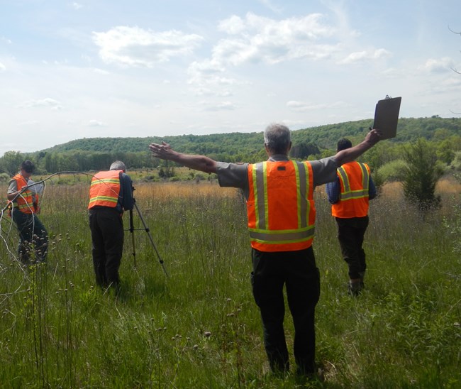 Visual Resources Inventory at Delaware Water Gap National Recreation Area A team of 4, evaluate a view at Delaware Water Gap National Recreation Area. A man stands with his both arms out to show the boundaries of the view. On man looks into a camera on a tripod. Other team members are looking at the view of a hill.