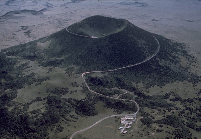 A nearly perfectly-shaped cinder cone rises more than 1000 feet above the surrounding landscape. A road winds around the volcano from the base to the top.
