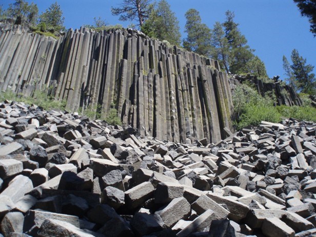 A wall of hexgonal rock columns extend up to 60 feet. Broken columns of the gray rock lie at the base of the wall.