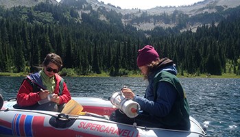 Image of two individuals handling scientific instruments in a raft floating on a lake.
