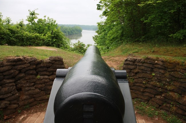 A large, black, iron cannon is pointed toward a river.