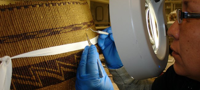 lt= A technician uses delicate tools to repair a woven basket