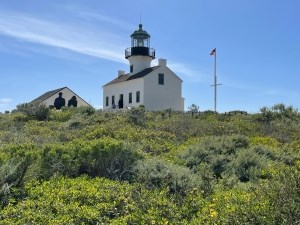 A colonial style light house stands on a hilltop next to an American flag and a foreground of sunflowers.