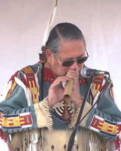 A man wearing Native American clothing plays a wooden flute into a microphone. A man wearing Native American clothing plays a wooden flute into a microphone.