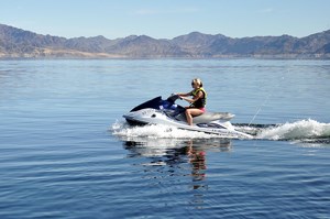 A woman on a personal watercraft on a lake with desert landscape in the background.