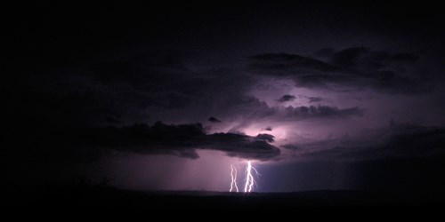 Lightning flashes turn the sky purple as they backlight black clouds in a dark night sky