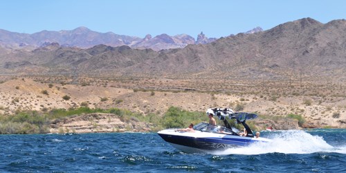 People ride in a motor boat on blue water with desert hills in the background