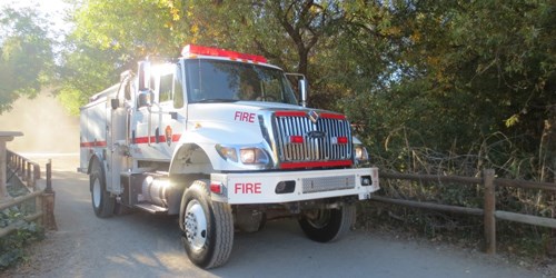 A large white and red fire engine on a road bordered by fence and trees