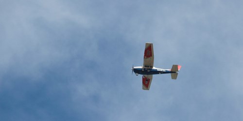A red, white, and blue fixed-wing propeller plane flies in a blue sky