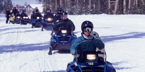 A group of people with helmets driving snowmobiles across the snow